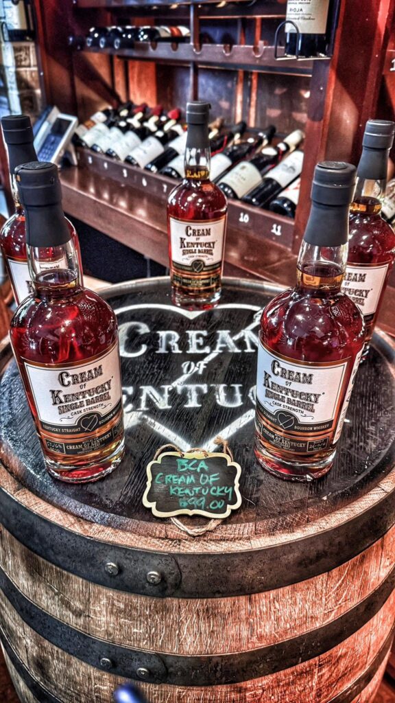 Cream of Kentucky Single Barrel #00177 bottles displayed on a whiskey barrel at Mash & Vine Market in Little Rock, Arkansas